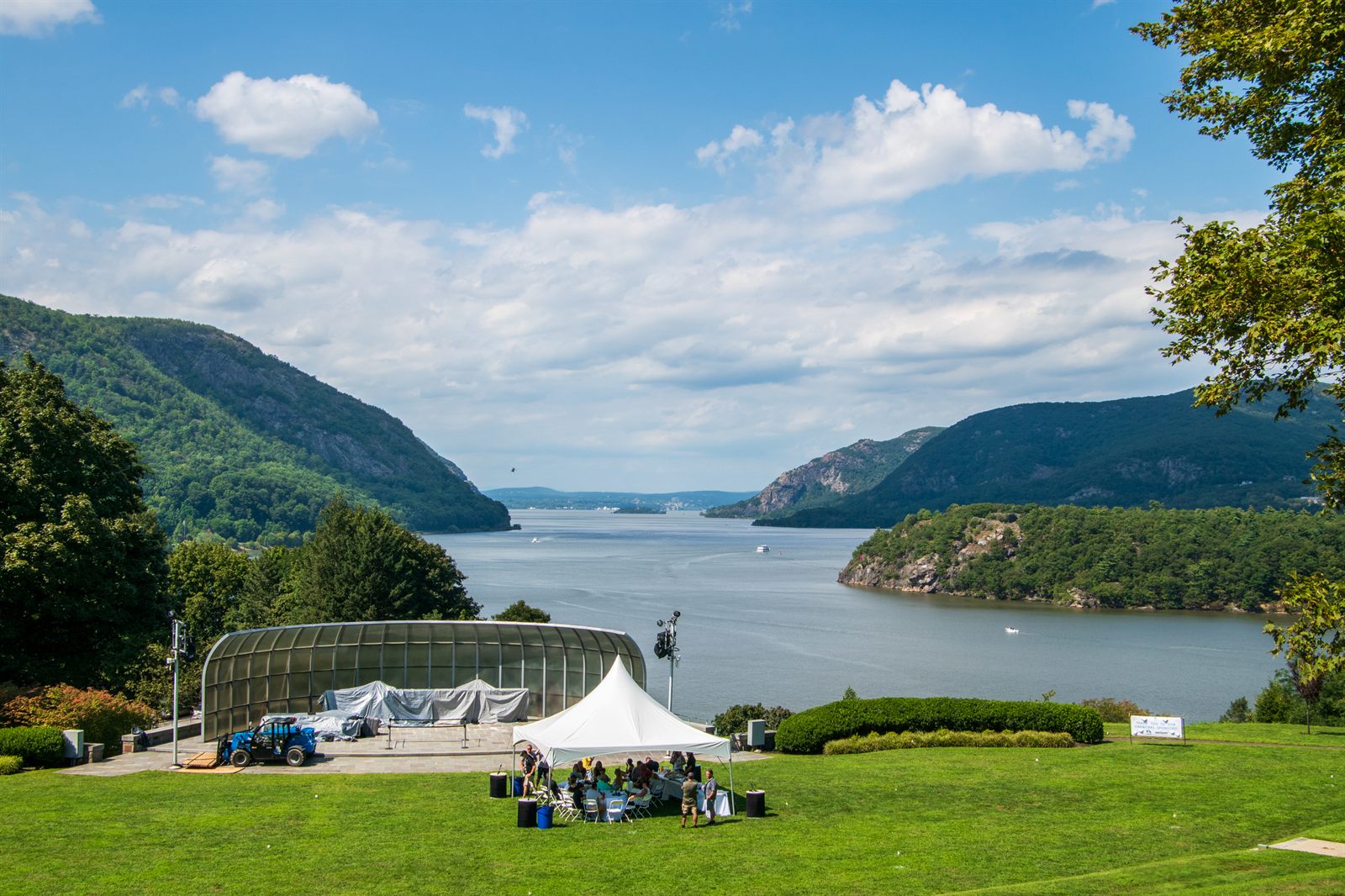 The Hudson River winding between steep wooded mountains, seen from a lawn with a white tent